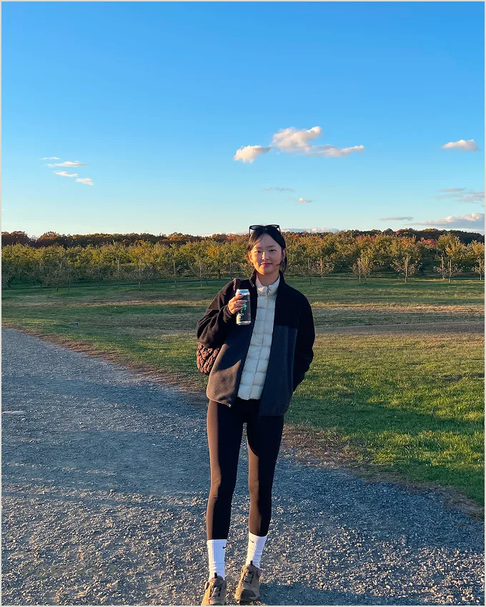 Yeseul Namgung standing on a gravel path in an orchard at golden hour